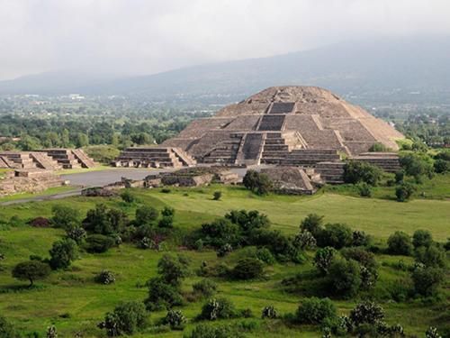 Ancient stepped pyramid ruins rising over green fields under a hazy sky