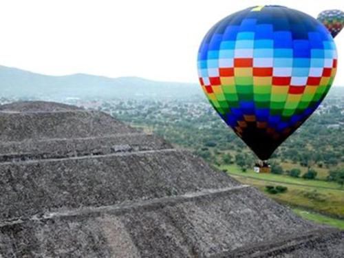 Colorful hot air balloon flying near stepped stone pyramid ruins in a green valley