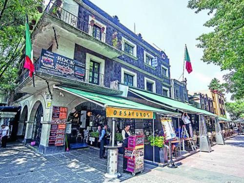 Street-side restaurant with green awnings and outdoor seating on a sunny corner.