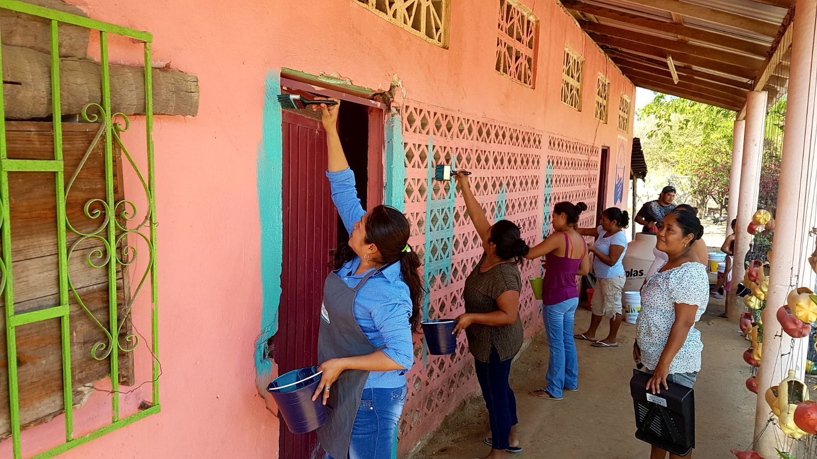 People standing outside a pink building, looking into a window and doorway during an activity.