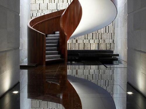 Modern spiral staircase with wood and white panels in a sleek interior, reflected on a glossy floor