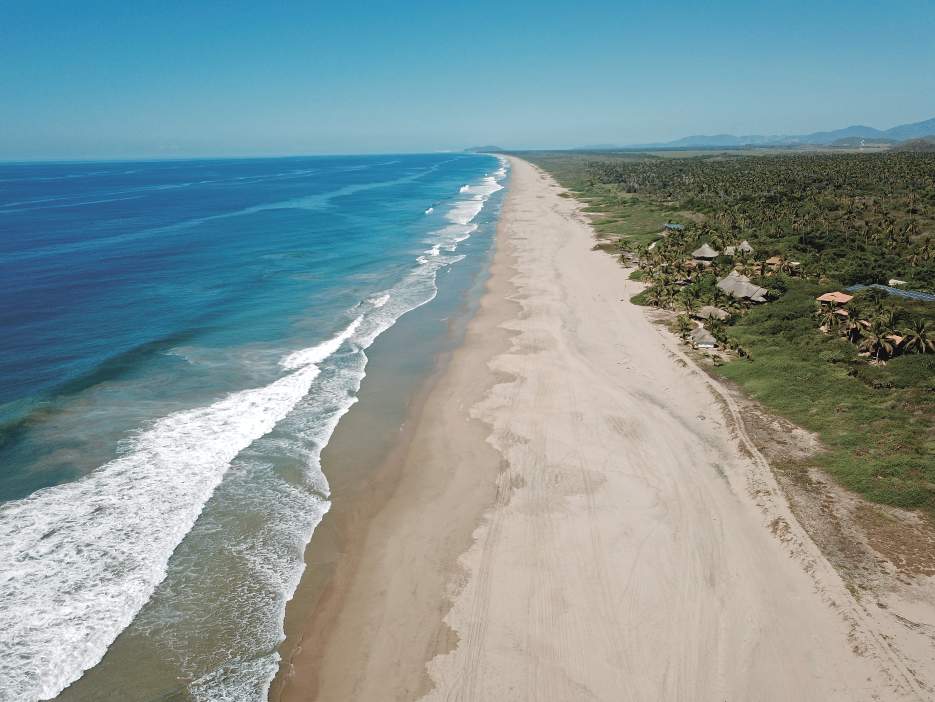 Aerial view of a long sandy beach with blue ocean and waves beside green coastline