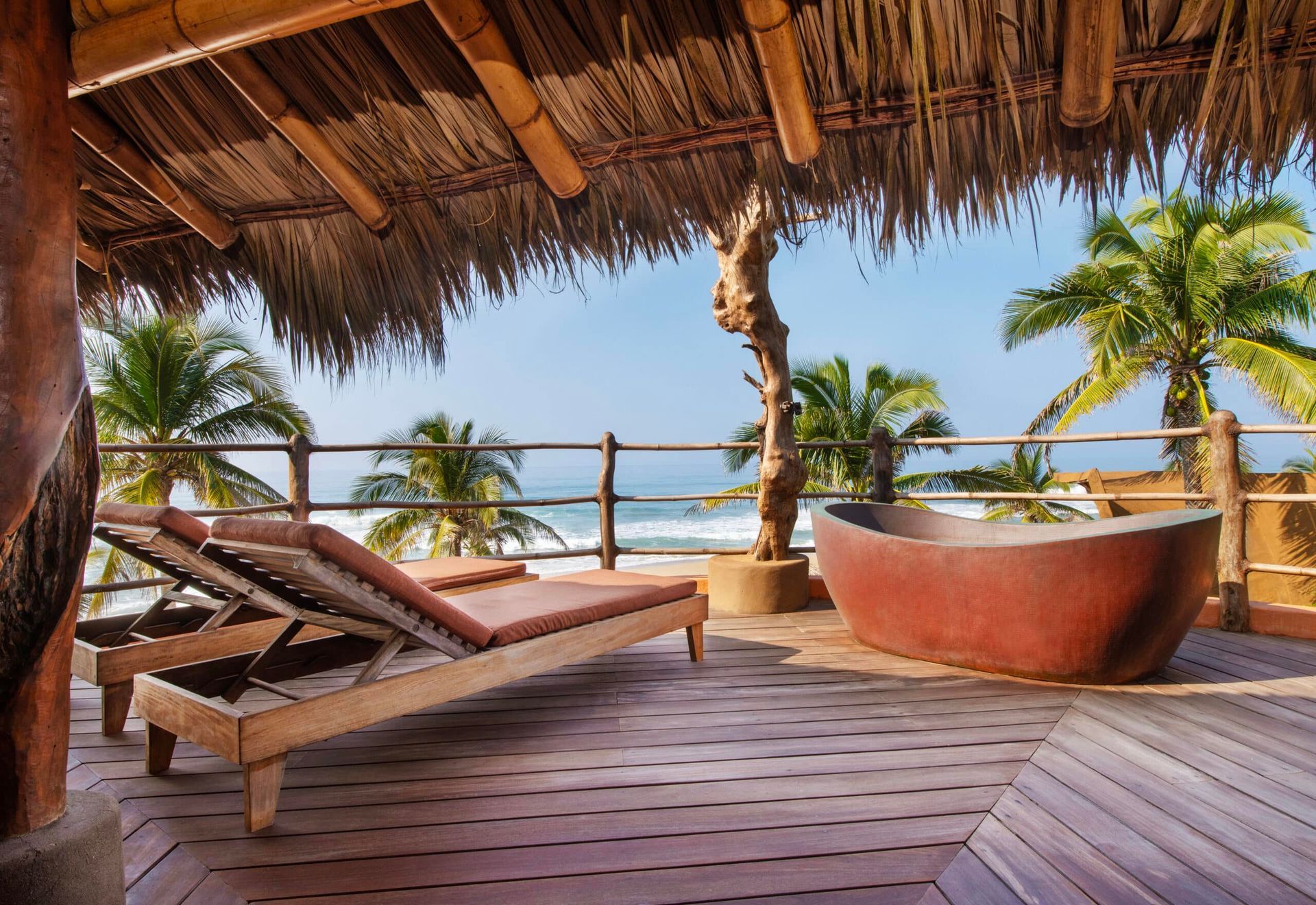 Tropical beach lounge with wooden deck, sunbeds, thatched roof, and ocean view