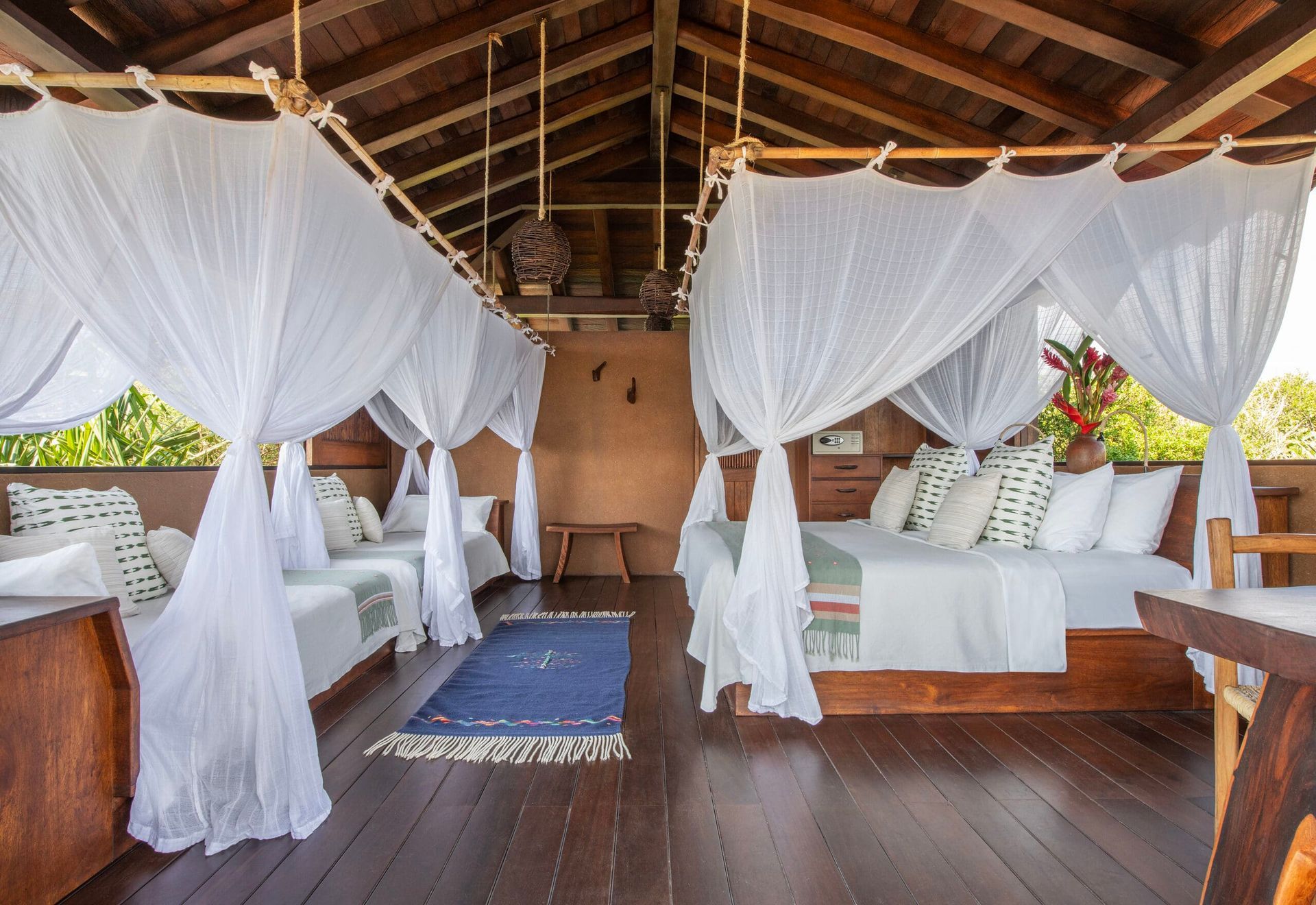 A room with four beds and mosquito nets hanging from the ceiling.
