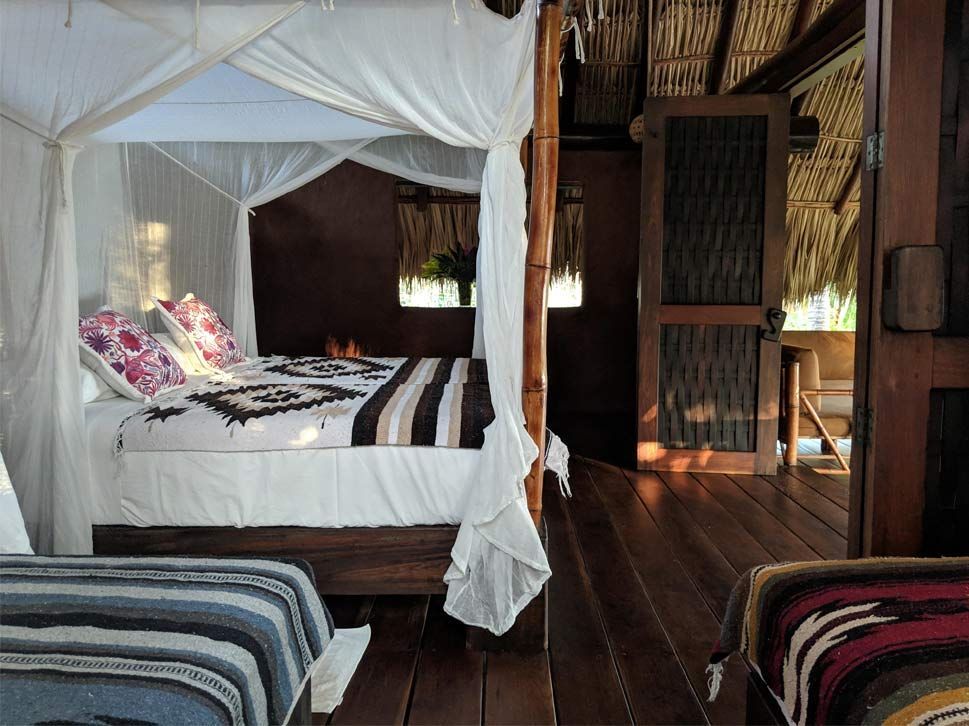 Rustic bedroom with a white canopy bed, striped bedding, and wooden walls and floor