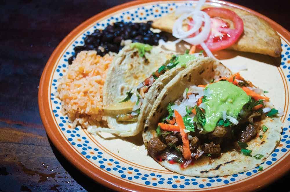 Plate of tacos with rice, beans, and garnishes on a patterned dish.