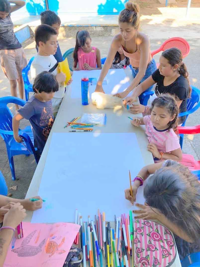 Children gathered around a table outdoors, drawing and coloring with markers and pencils.