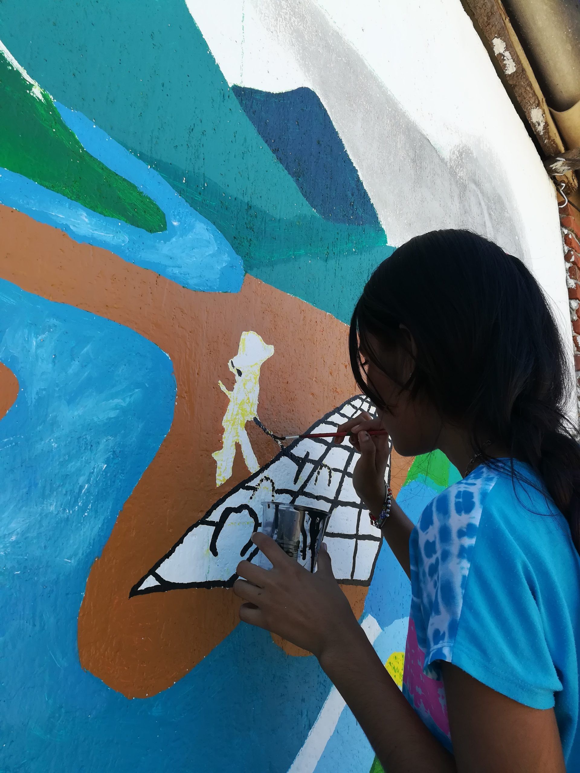 Person painting a colorful mural on a wall with blue, brown, and green shapes