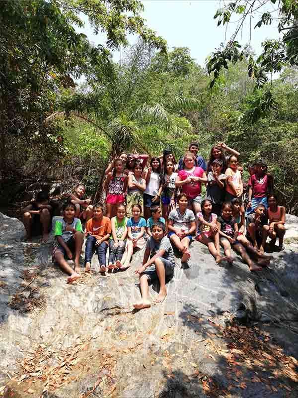 Group posing on a rocky ledge in a forested outdoor setting, with lush green trees around them