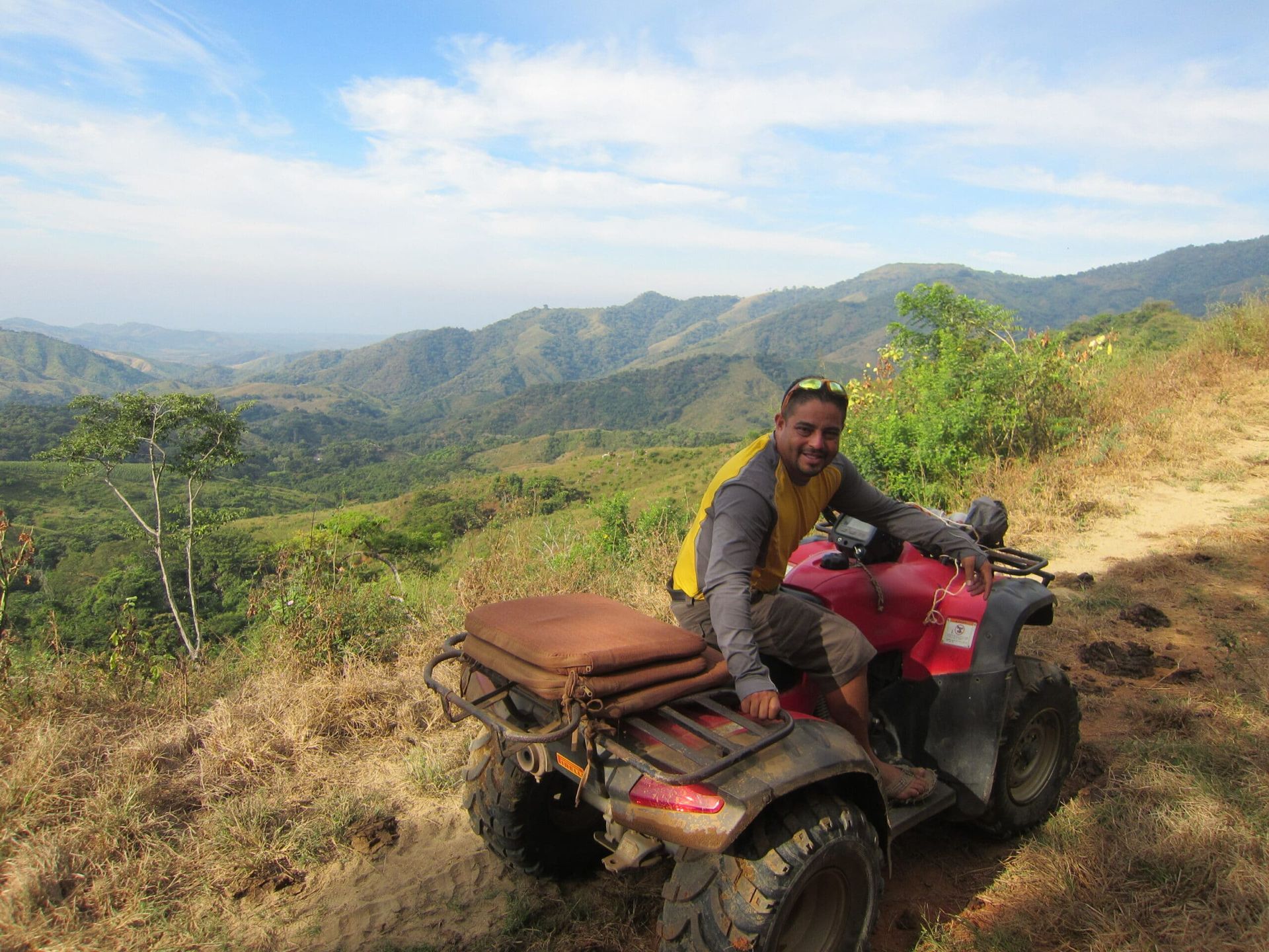 Person on a red ATV on a hillside trail overlooking a green mountain valley