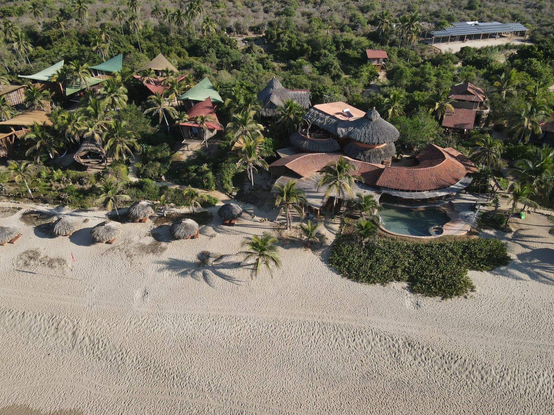 Aerial view of a tropical beach resort with palm trees, huts, and white sand by the shoreline