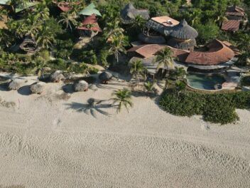 Aerial view of a tropical beach resort with palm trees, round-roof villas, and a sandy shoreline