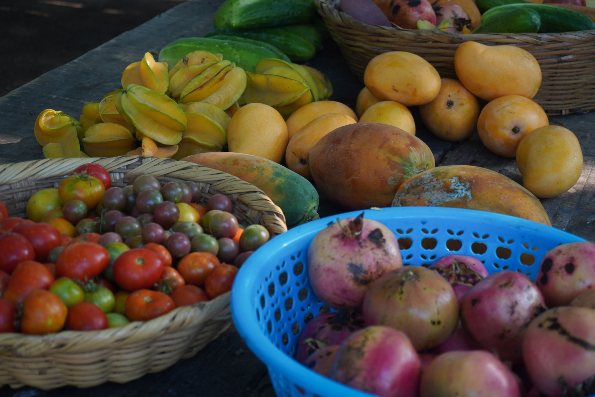 Assorted tropical fruits in baskets at a market stall, including mangoes, tomatoes, and dragon fruit.