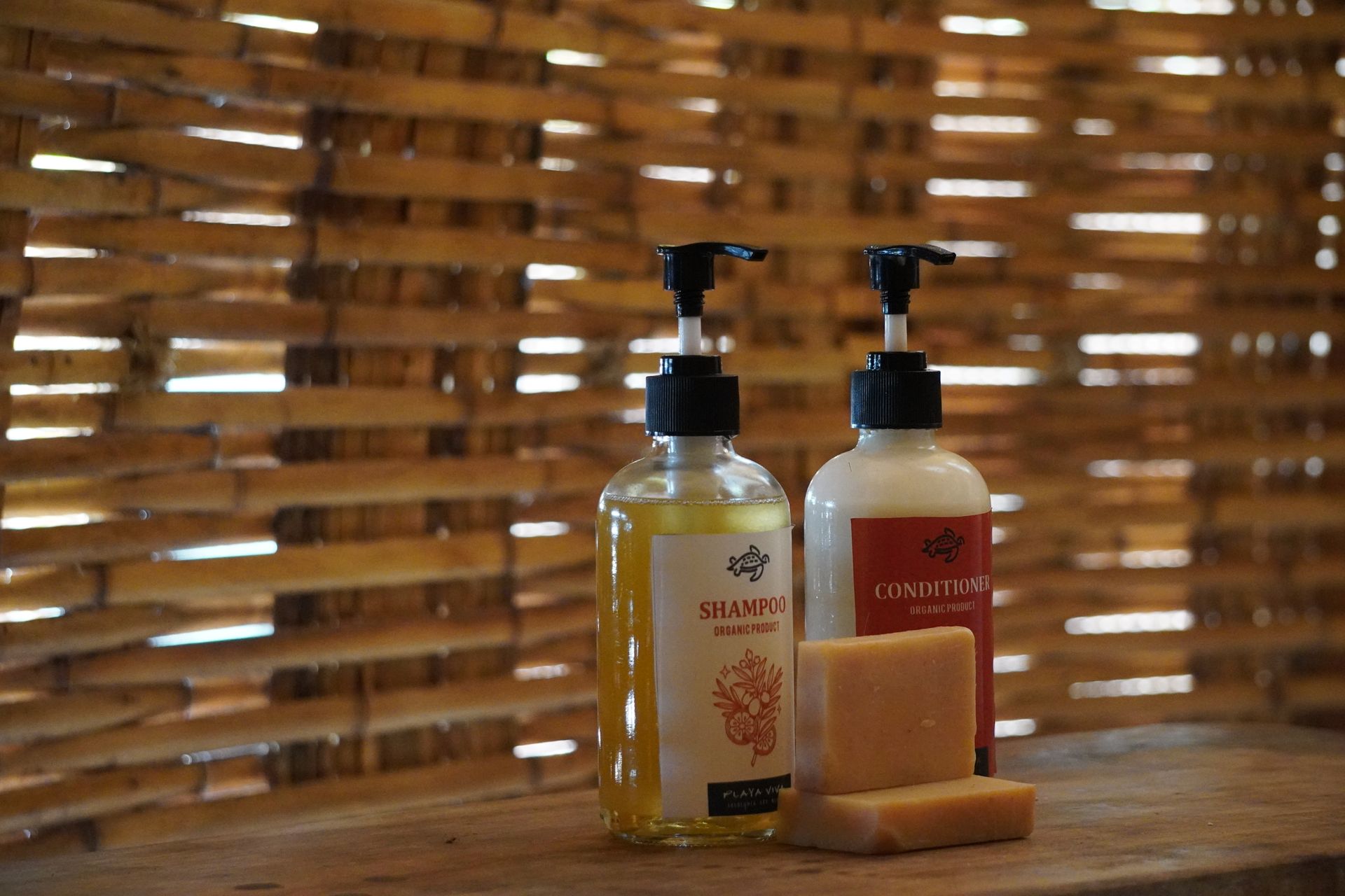 Two amber soap bottles and a bar of soap on a wooden table before a woven backdrop