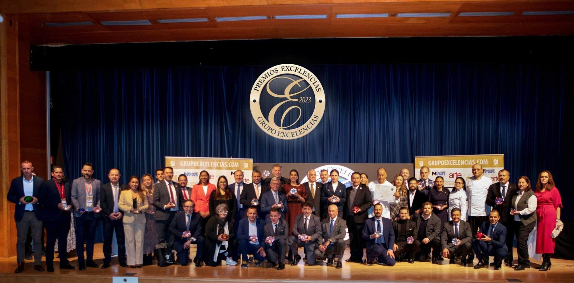 Large group posing on a stage with a dark blue curtain and circular emblem backdrop.