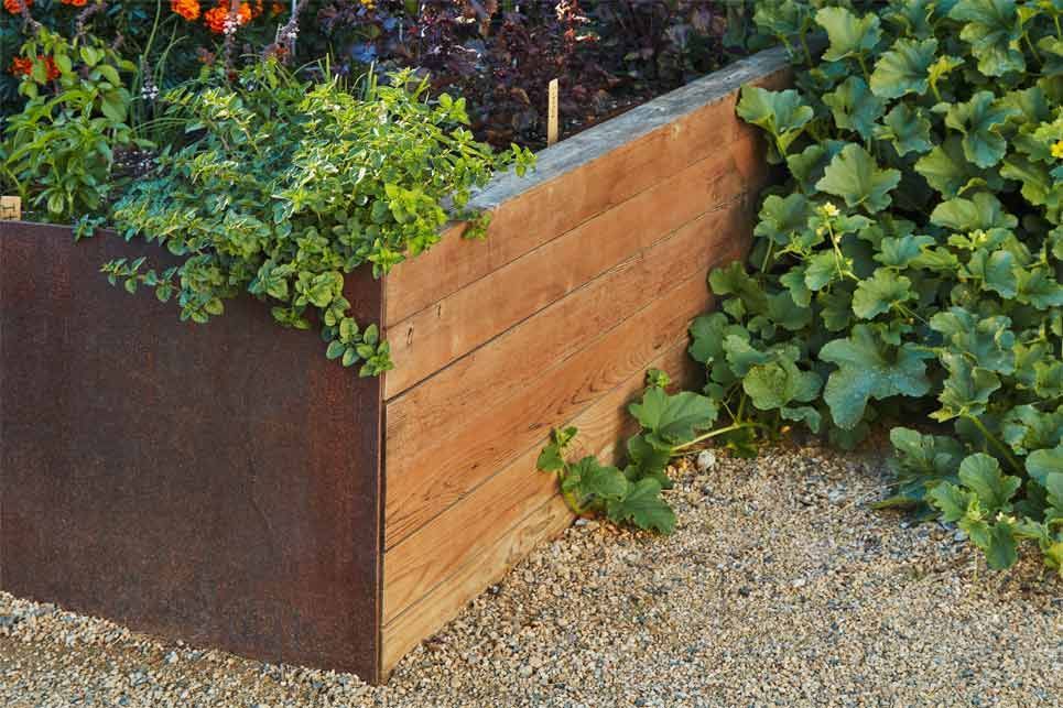 Wooden planter box with green plants on a gravel patio