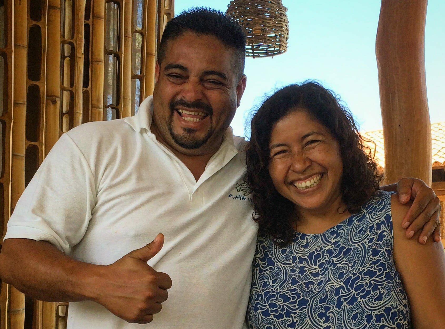 Two smiling people posing together outdoors, one giving a thumbs-up