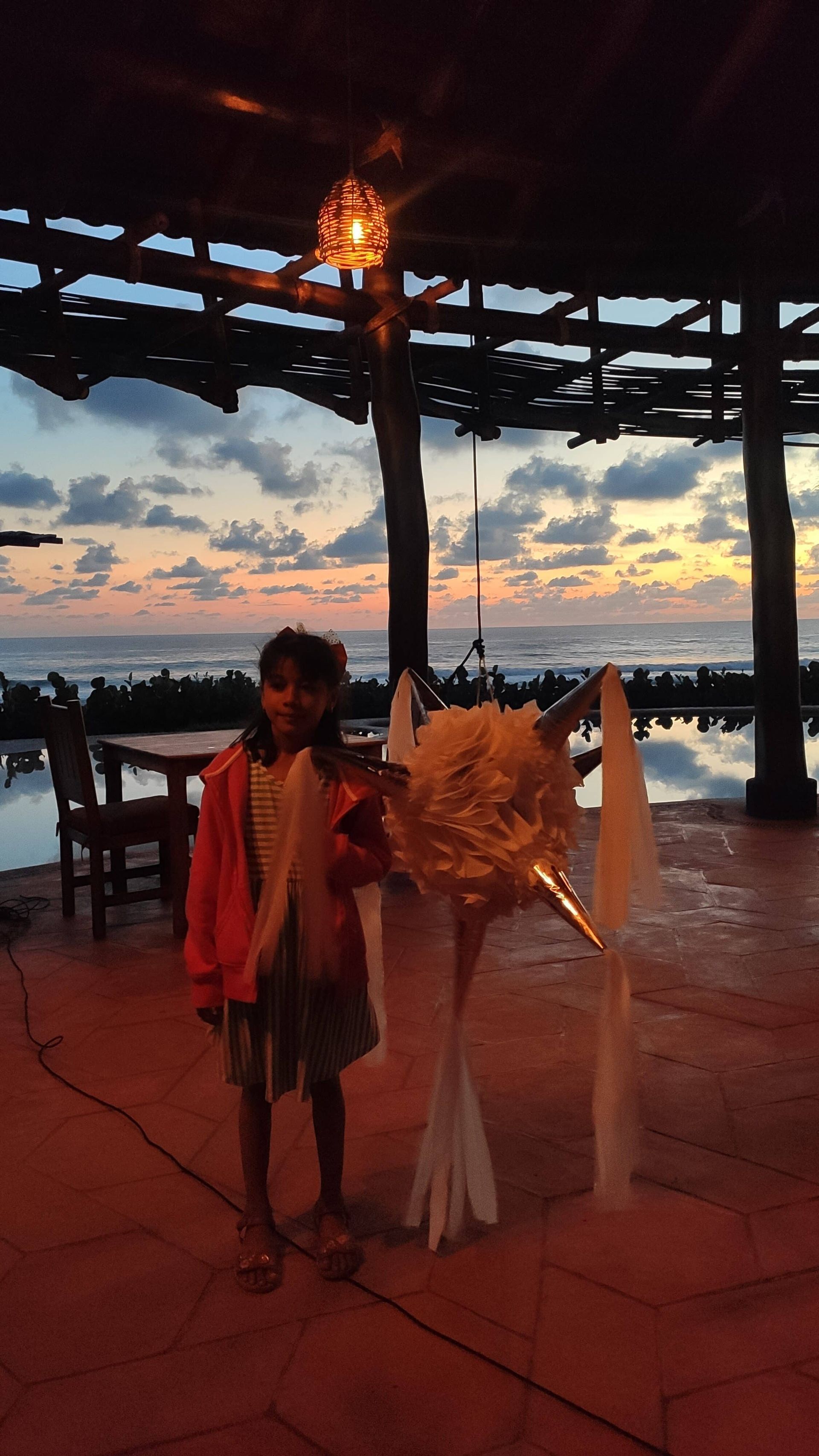Person standing with a white horse costume at sunset under a pavilion by the water