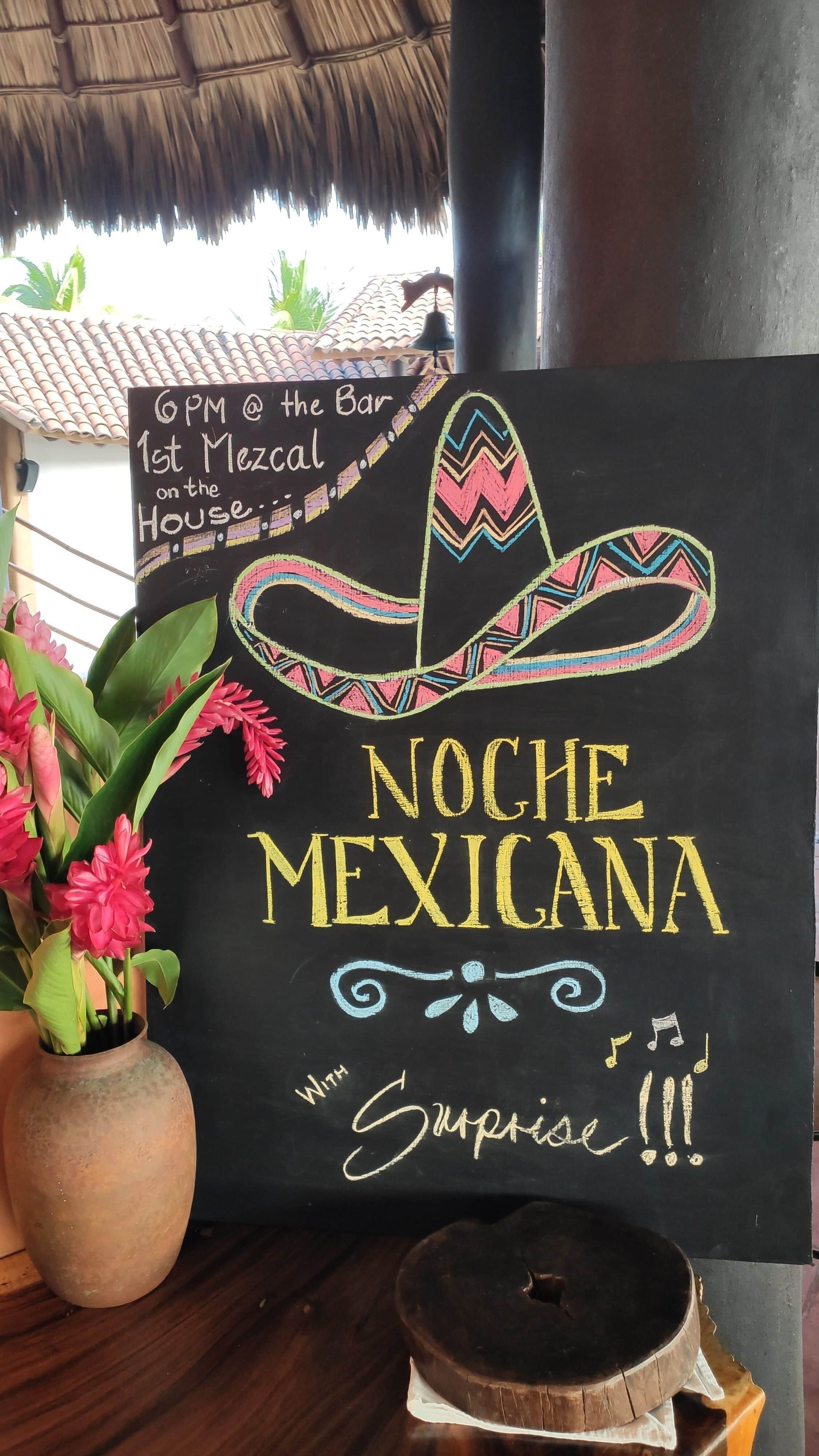 Mexican-themed sign with sombrero and flowers reading “Noche Mexicana” and “Somos” on a dark background