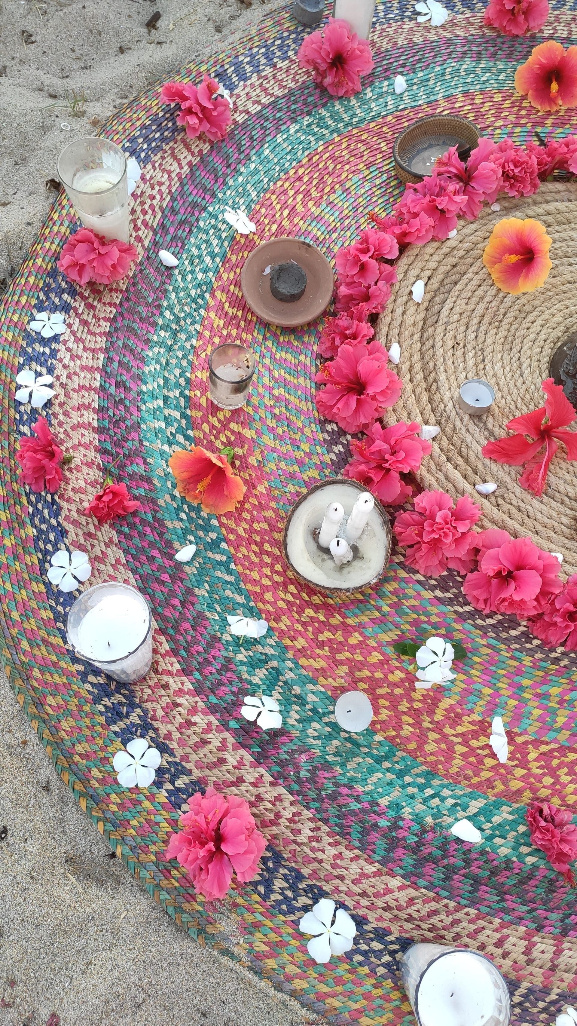 Circular floral rangoli in pink, red, white, and green flowers with candles on sand.