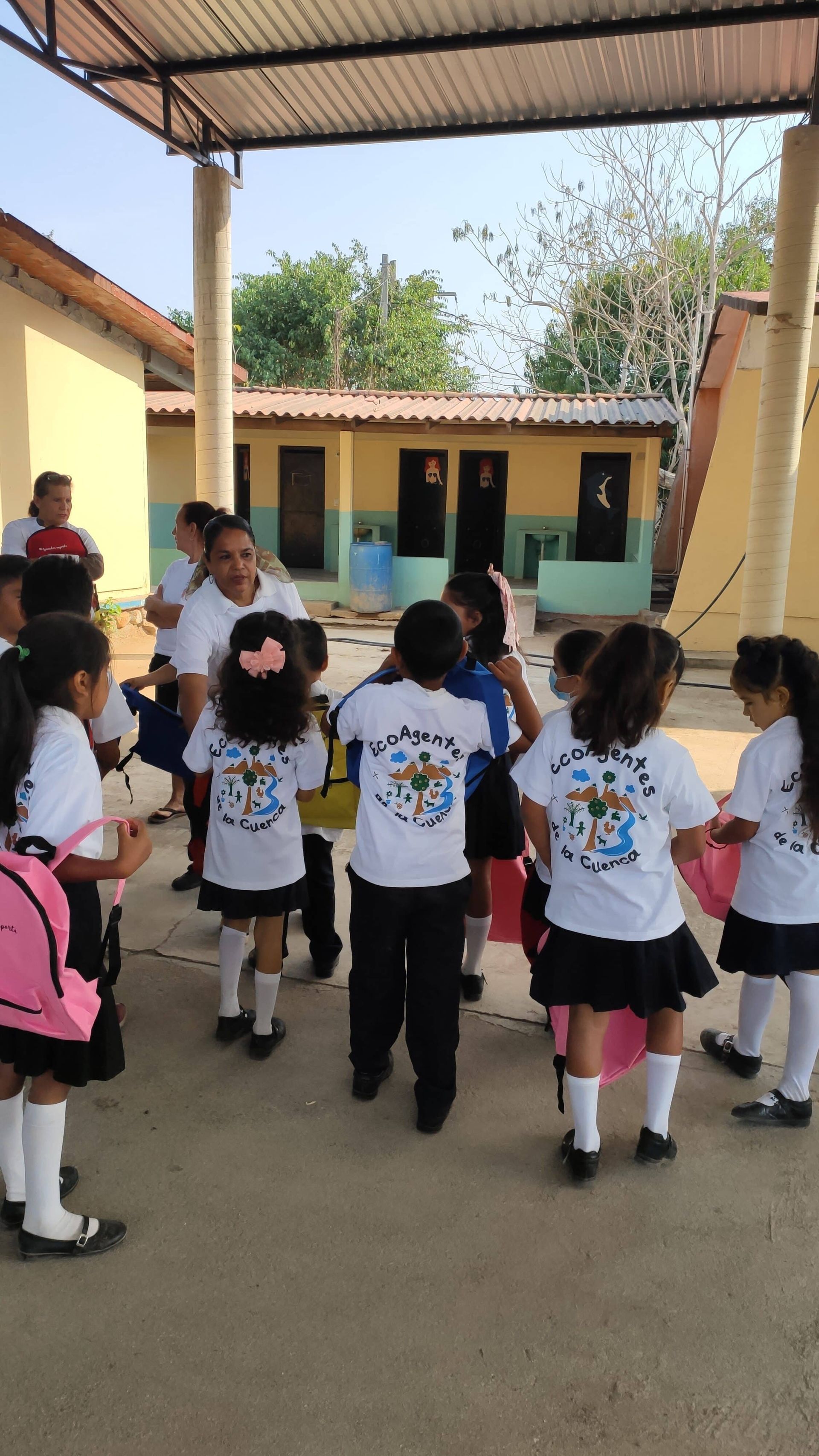 Children in white shirts gather in a covered school courtyard during an outdoor activity.