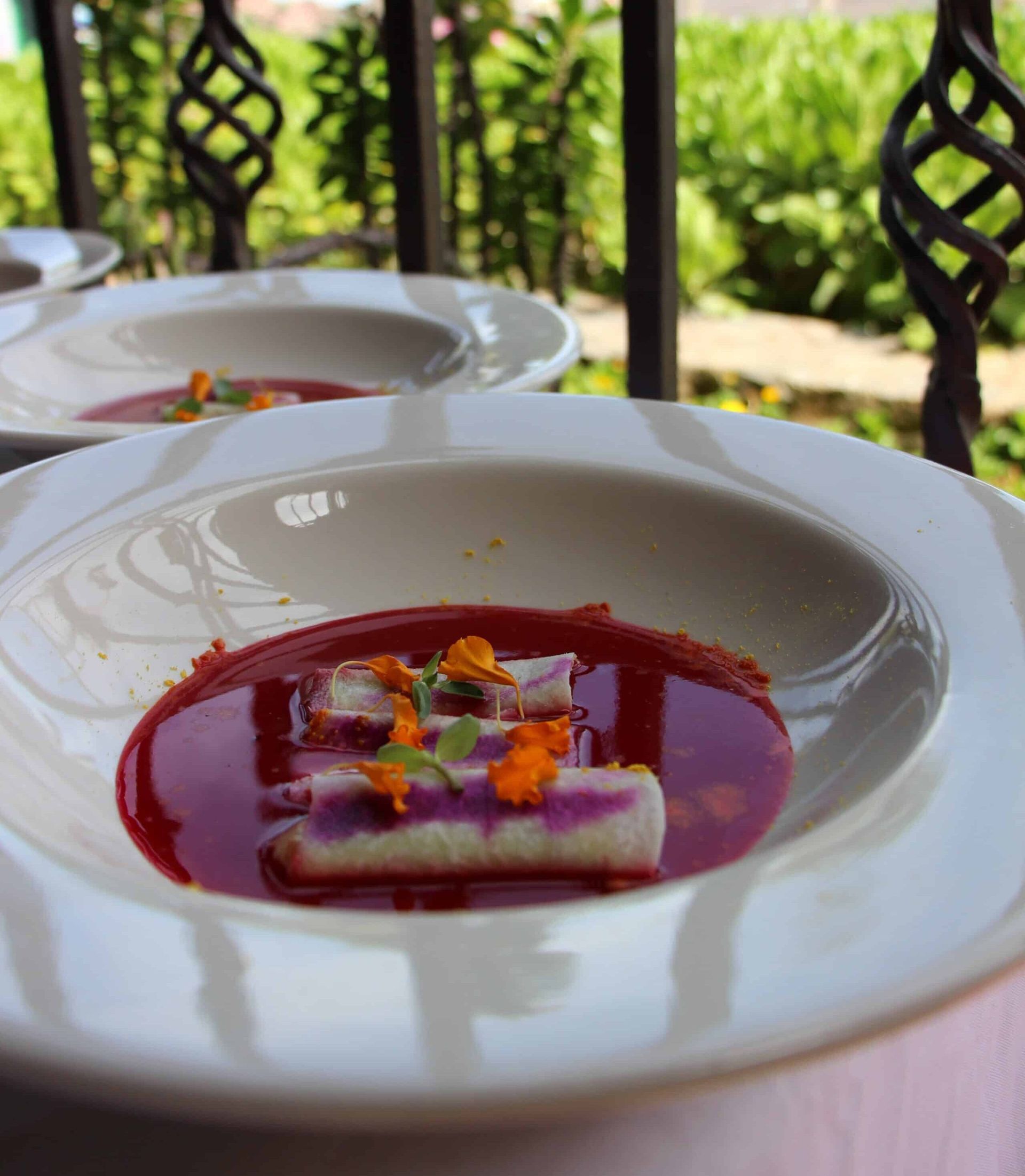 Dessert on a white plate with red sauce and edible flowers on an outdoor table.