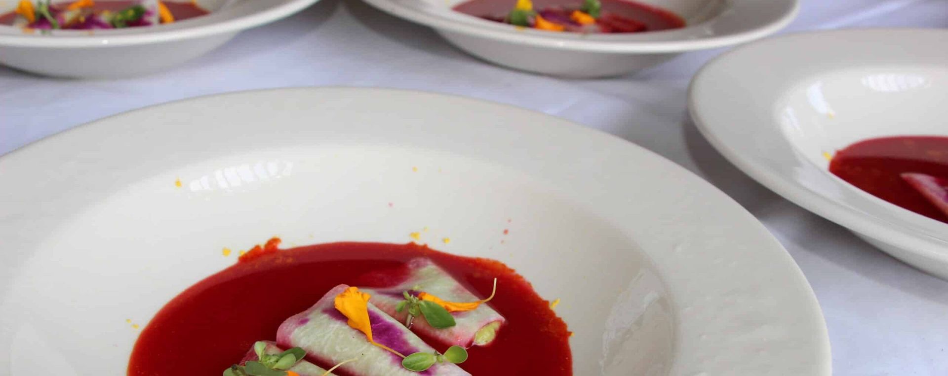 Plated red soup topped with colorful garnish on a white table setting