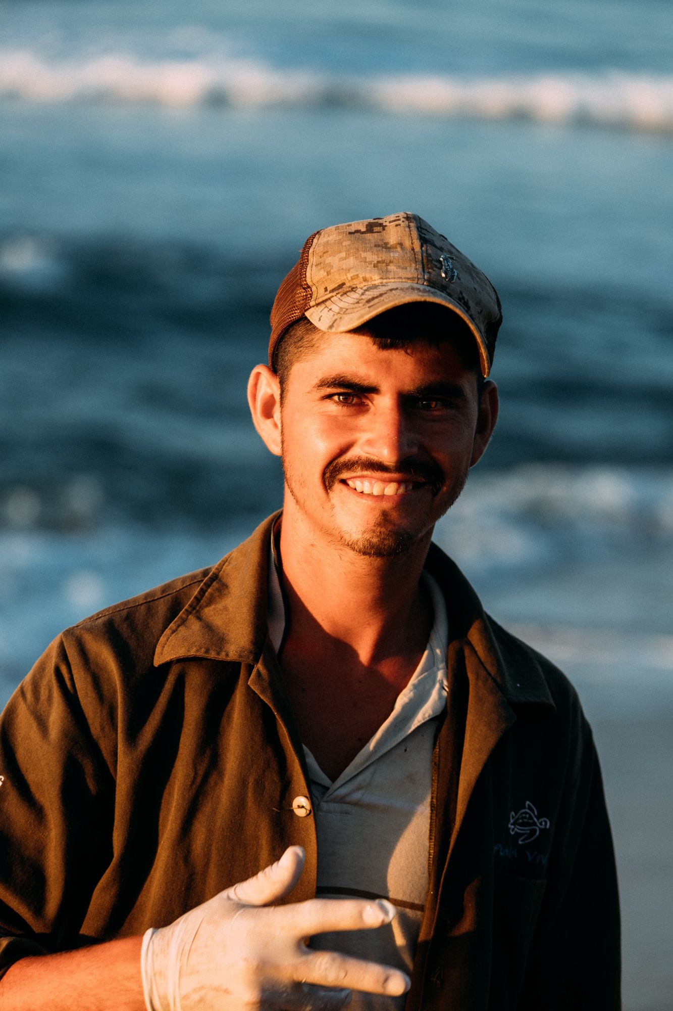 Smiling man in a cap standing at the beach with ocean waves behind him