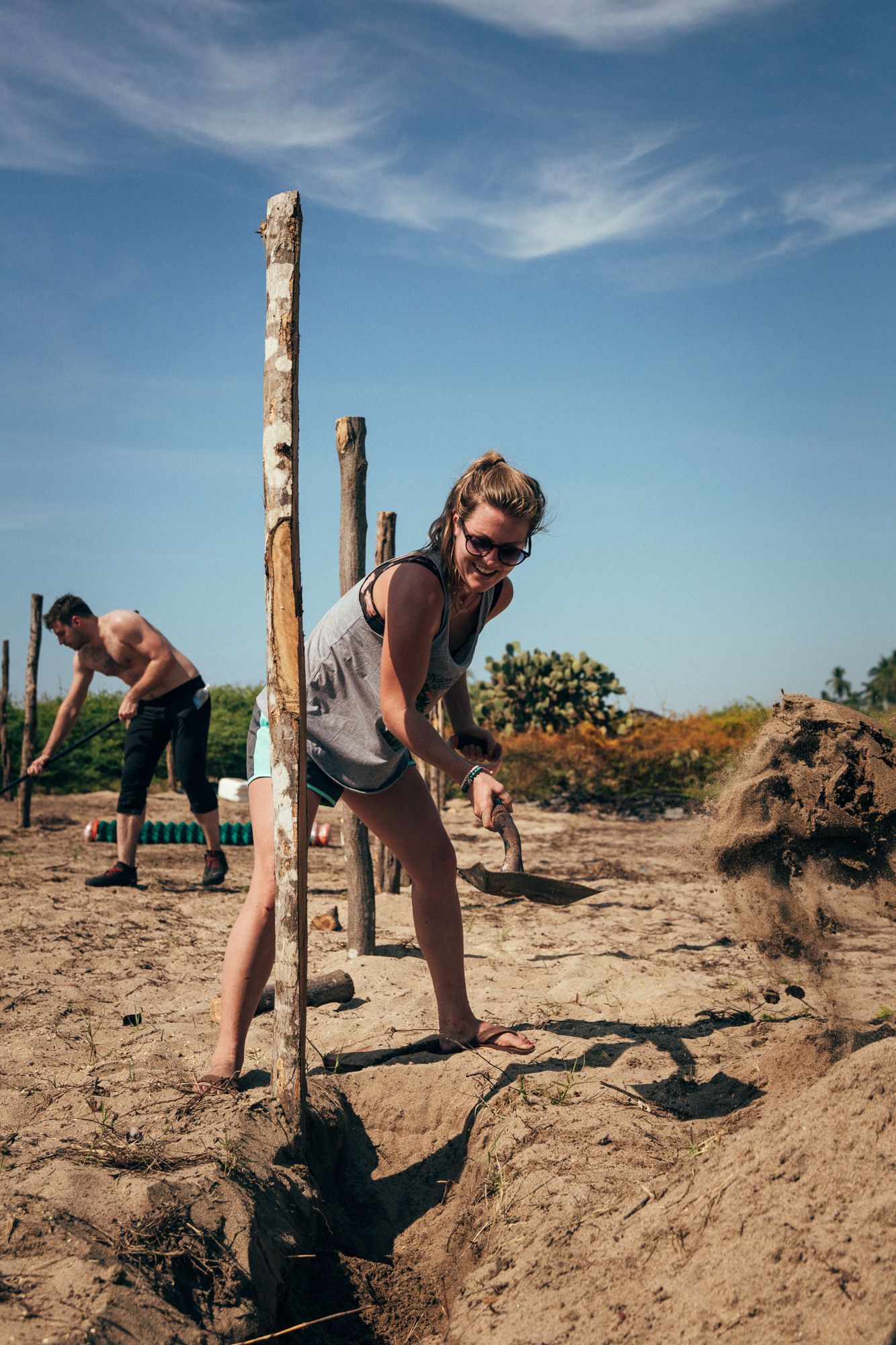 People digging soil with shovels in a dry outdoor field under a blue sky