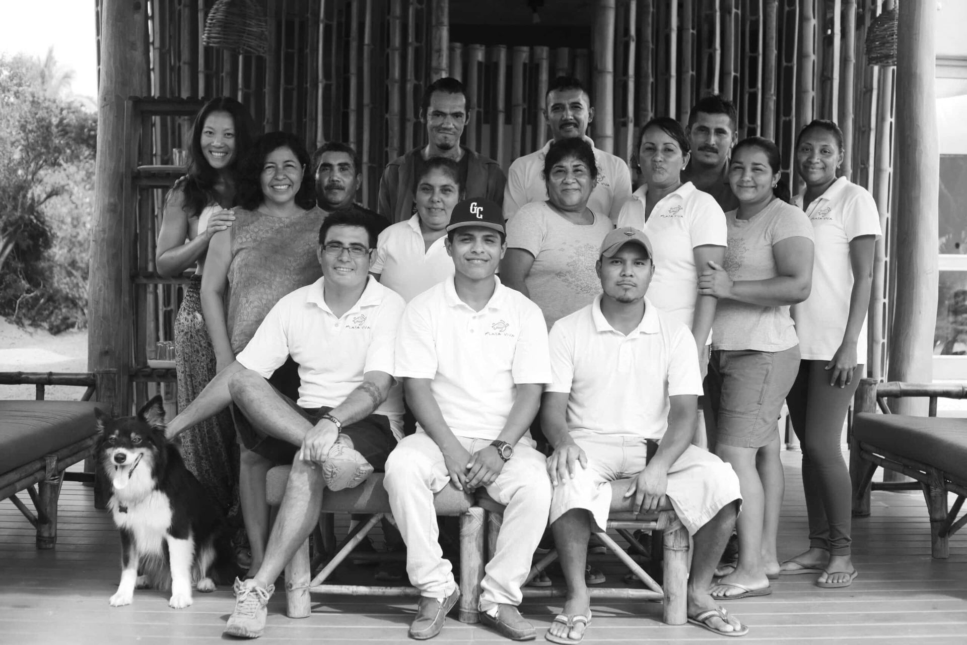 Group portrait of people posing on a wooden porch with a dog in front, in black and white.