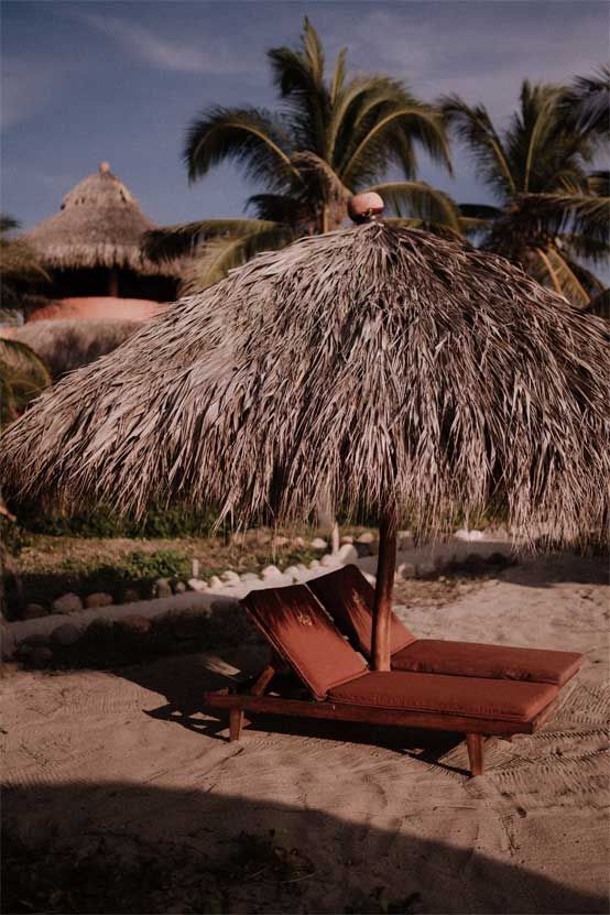 Thatched beach umbrella shading a red lounge chair on a sandy tropical resort beach