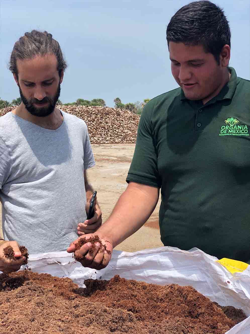 Two men inspecting soil on a white tarp outdoors under a bright sky