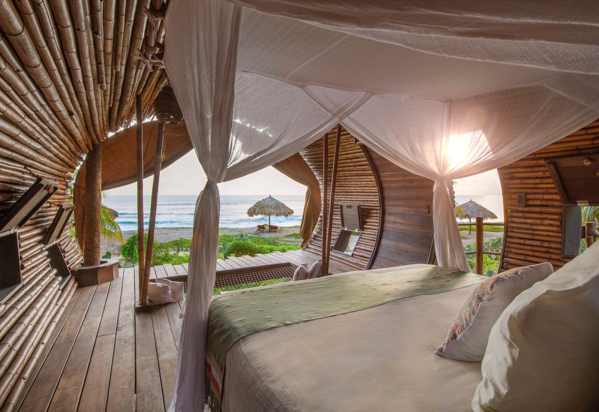Beachfront thatched bungalow bedroom with canopy bed and ocean view through open wooden doorway