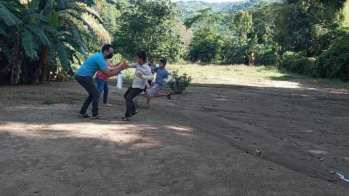 Three people playing in a dirt clearing surrounded by lush green trees and plants.