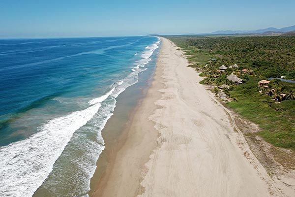 Aerial view of a long sandy beach with turquoise waves and green coastline under a clear sky