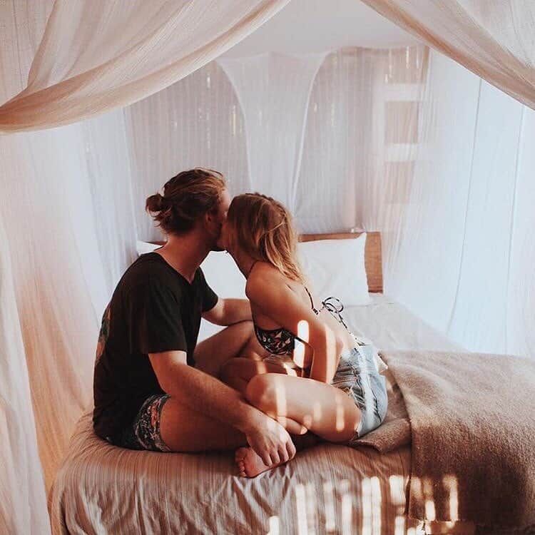 Couple kissing on a bed in a soft, white-draped bedroom