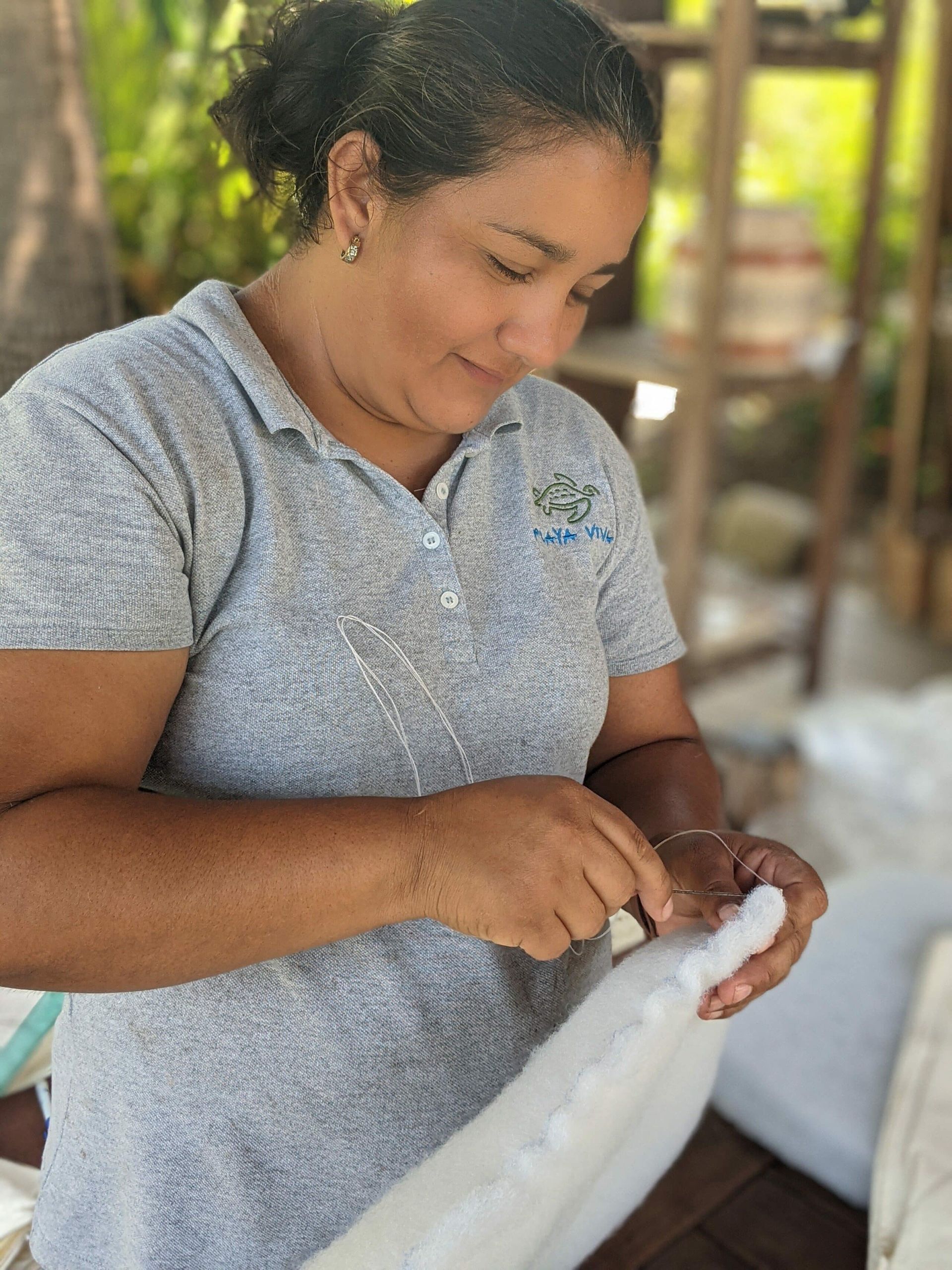 Woman in a gray polo shirt sewing white fabric outdoors.
