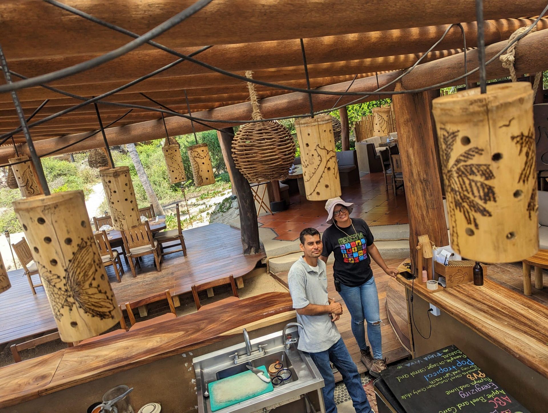 Two people standing in a rustic indoor exhibit with hanging carved wood art panels.