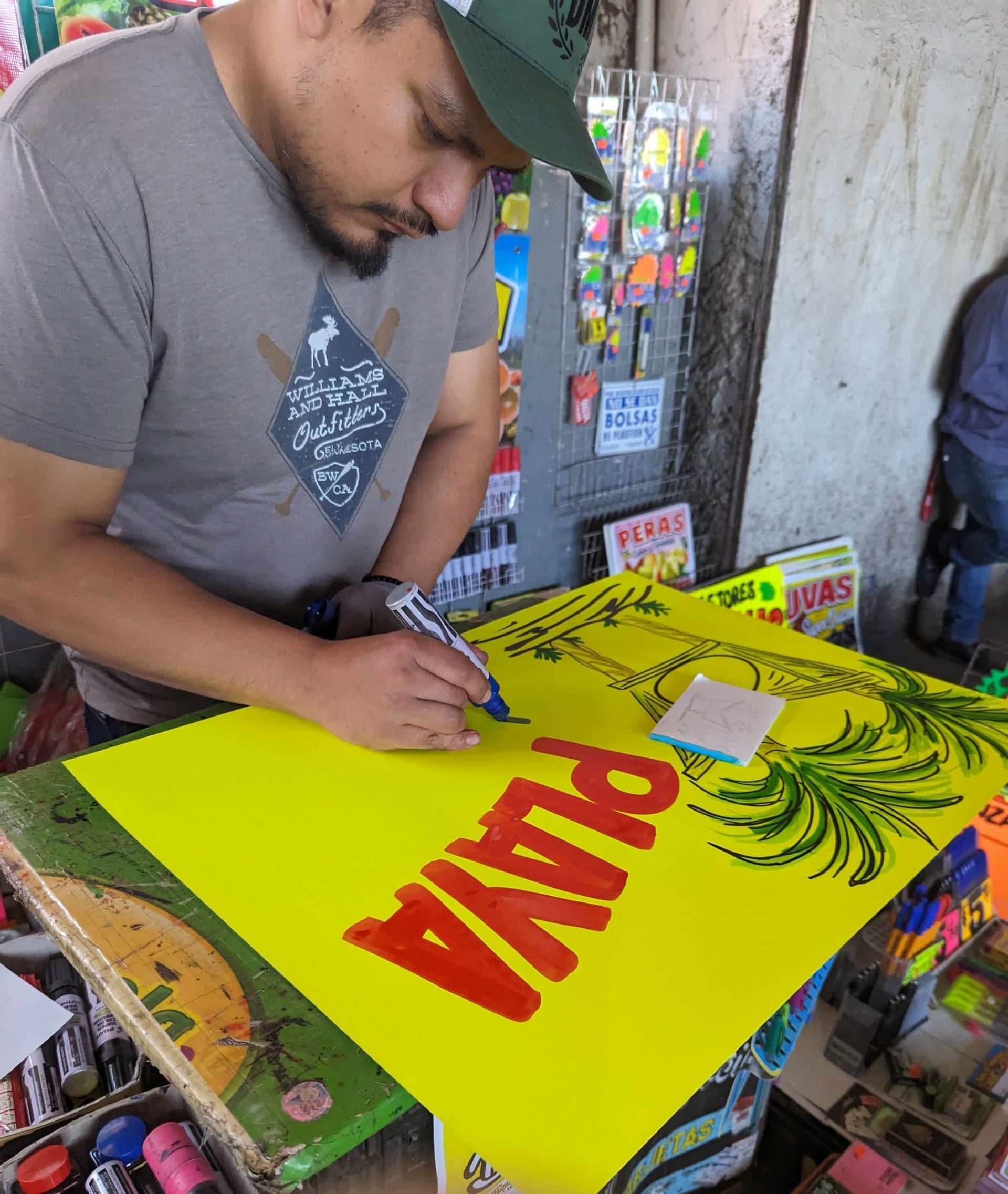 Man signing a bright yellow poster with red lettering at a street-side stall