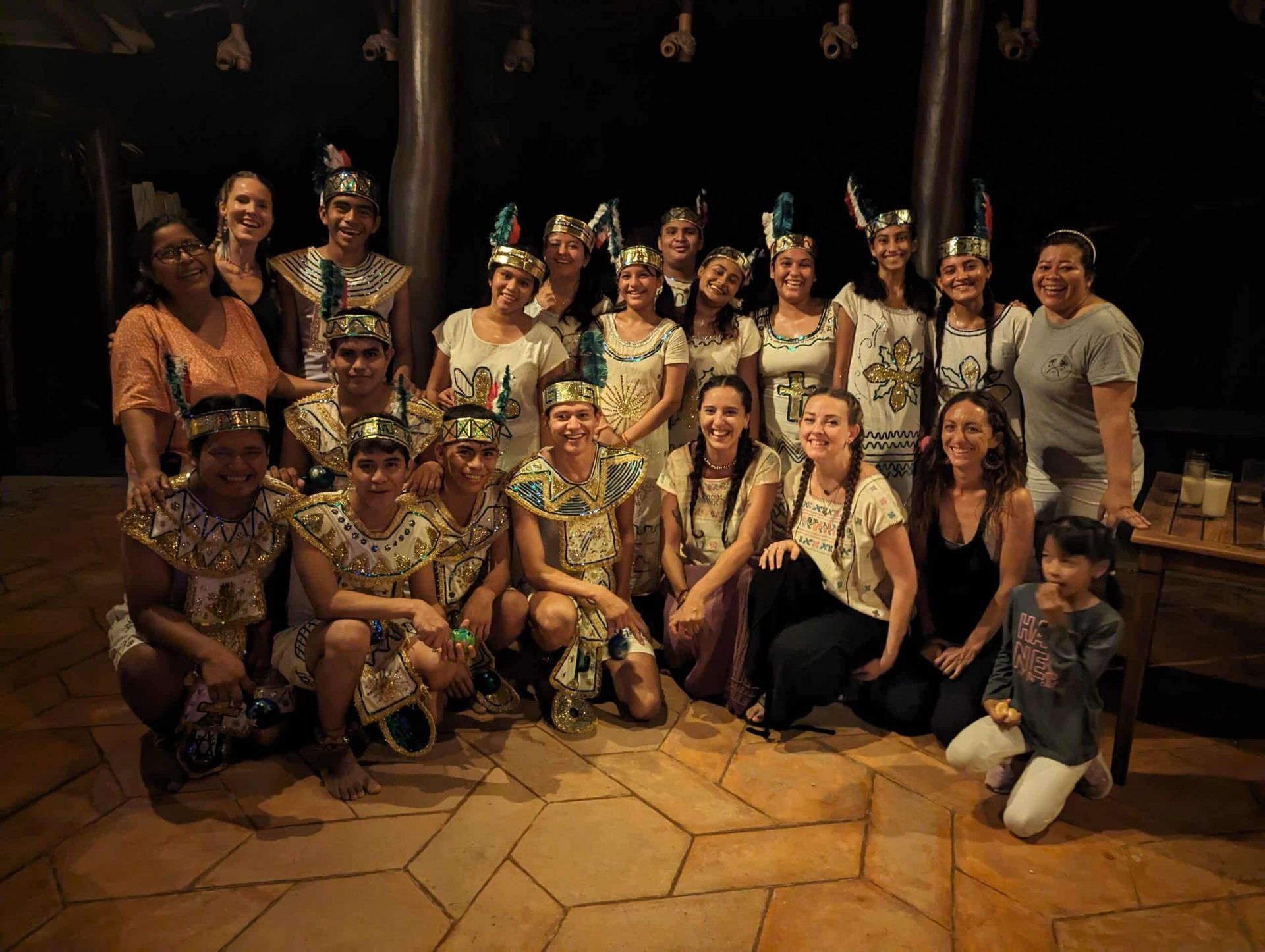 Group posing indoors in festive traditional costumes, smiling and kneeling on a tiled floor