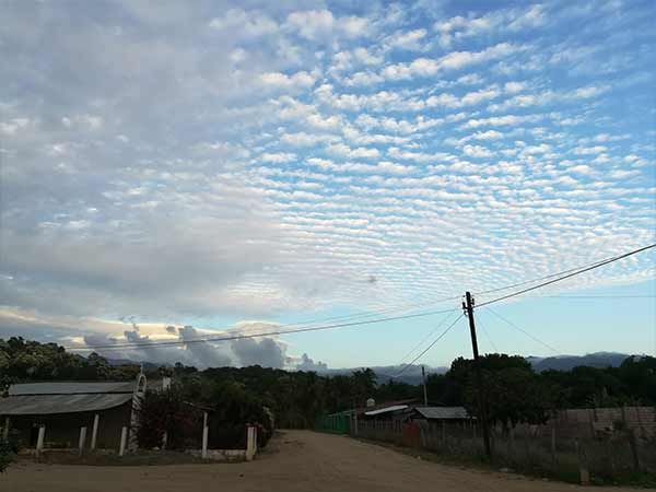 Cloudy sky with rippled clouds over a rural road, houses, trees, and a utility pole at sunset