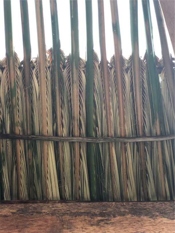 Vertical woven reed fence with tan and green stalks against a brown ground