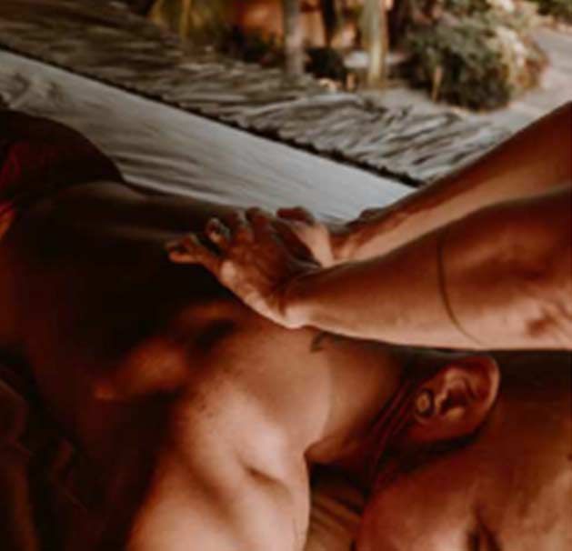 Person receiving a back massage on a bed with a light sheet, warm lighting.