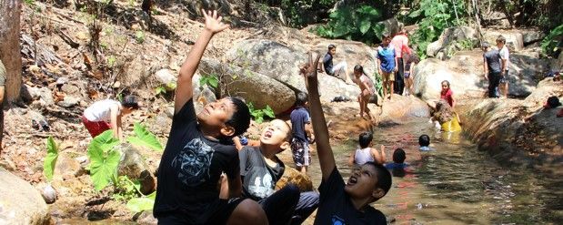 People wading in a rocky stream, reaching up to splash water outdoors.