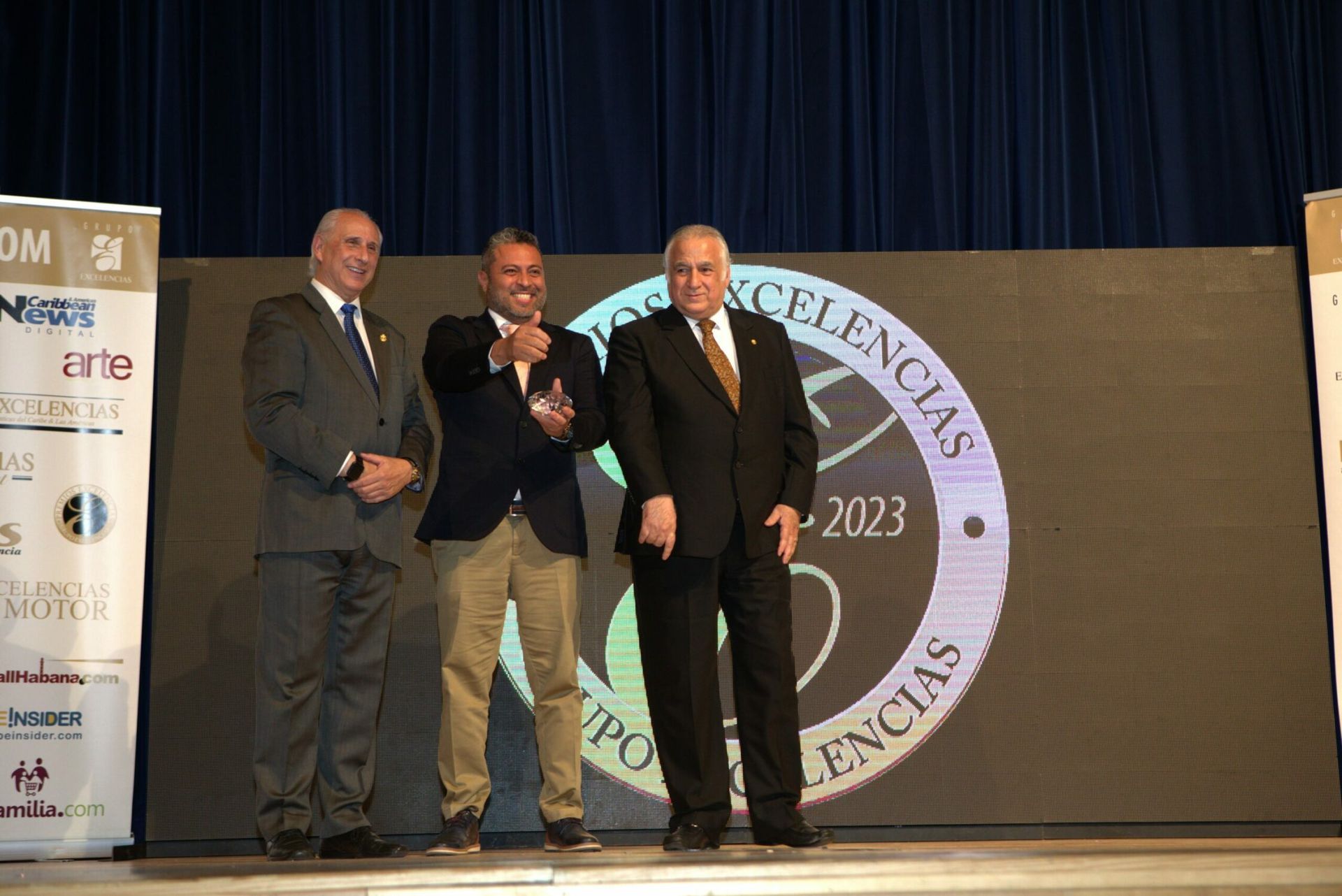 Three men in suits pose on stage beside a 2023 award backdrop