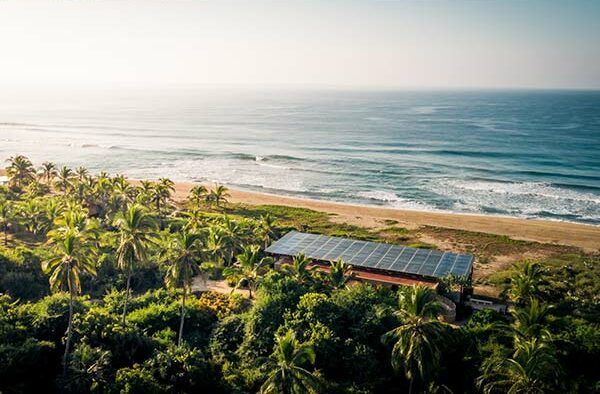 Aerial view of a tropical beach with palm trees, a small house, and the ocean at sunset.
