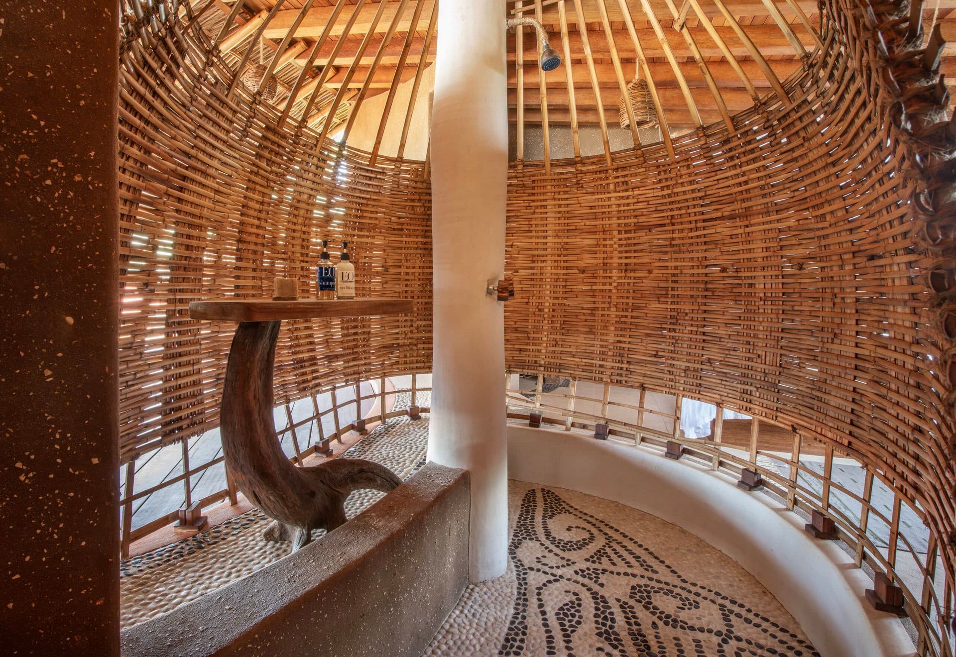 Curved woven wood interior with central white pillar and spiral stairs, lit by warm sunlight