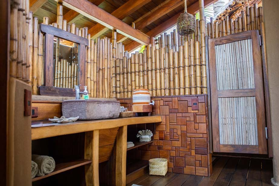 Bamboo bathroom interior with wooden sink counter, woven walls, and slatted doors under a pitched roof