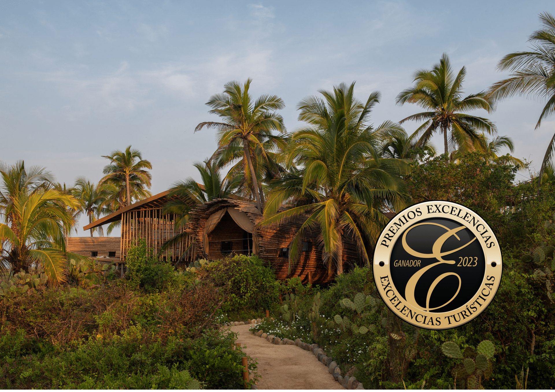 Tropical resort with palm trees, rustic huts, and a winding path under a clear sky