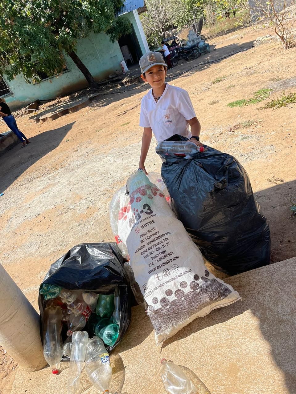 Person in a hat stands beside large bags of collected recyclables outdoors.